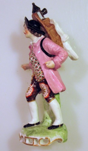 Photo of a ceramic figure representing an 18th century magic lantern showman with his lantern strapped to his back.